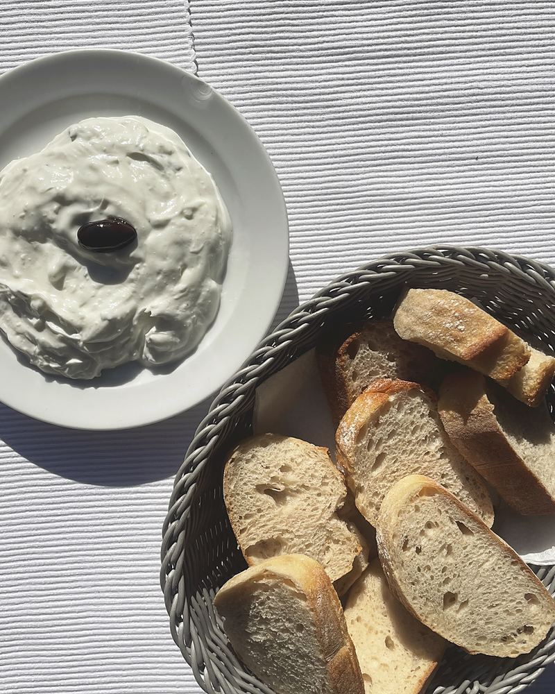 Zaziki mit einer Olive, daneben ein Korb mit frischem Weißbrot